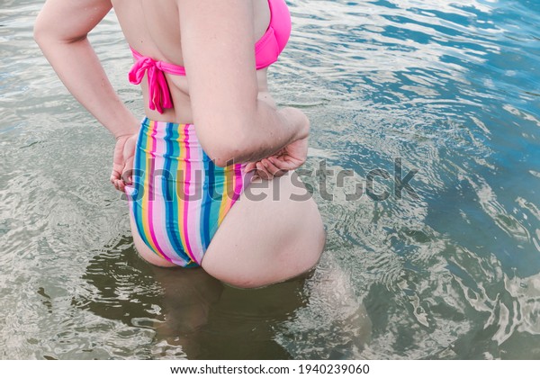 An\
anonymous woman adjusts her bikini bottom in almost waist deep\
water. Vacation getaway and summer fashion\
theme.