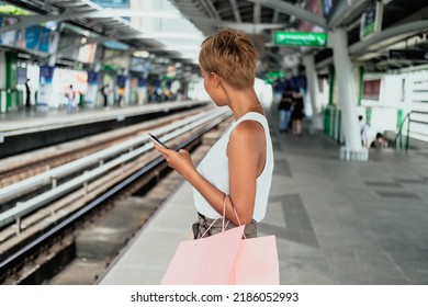 An Anonymous Woman Holding Shopping Bags And Using Mobile Phone While Standing At Railway Platform