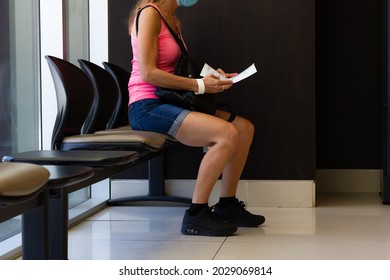 Anonymous Woman On Summer Clothes With Face Covering Sitting On Doctor's Waiting Room Reading Medical Report. Sickness, Ill Person, Patience, Social Distance, Health Care Delay Concepts