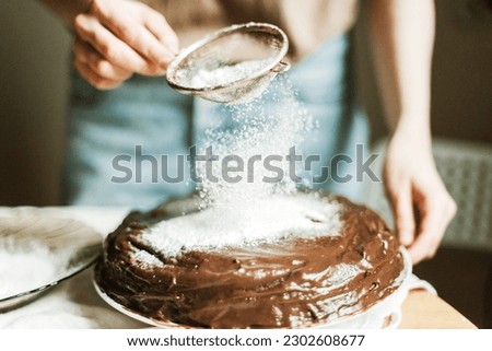 Anonymous woman pouring powdered sugar on chocolate cake