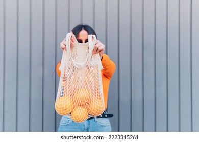 Anonymous woman showing reusable mesh bag with oranges to camera. Lagom culture and sustainability - Shutterstock ID 2223315261