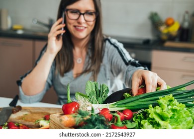 An Anonymous Woman Talking On A Mobile Phone While Making Healthy Lunch With Colorful Vegetables In The Kitchen