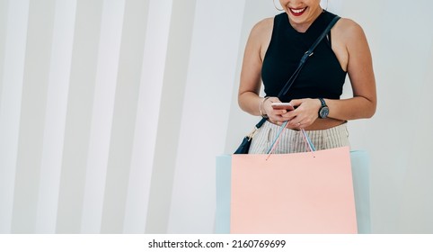 An Anonymous Woman Using Mobile Phone And Holding Shopping Bags While Standing In Front Of White Geometric Wall