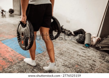 Anonymous young Asian man does farmers walk with plates at the gym focusing on grip strength, core stability, and full body endurance using weighted plates in functional exercise