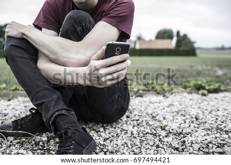 An anonymous young man or boy holding his phone and looking at it. A concept about struggling with yourself, being mentally and physically tangled up, autism, online bullying and suicide thoughts.