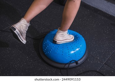 An anonymous young woman engaging in a core-strengthening workout as she balances on a Bosu Ball at the gym, focusing on fitness and stability.
