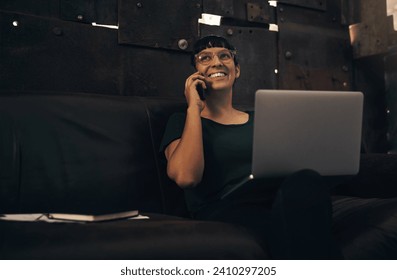 Another call, another happy client. Shot of a young woman using a laptop and smartphone while working at a foundry. - Powered by Shutterstock