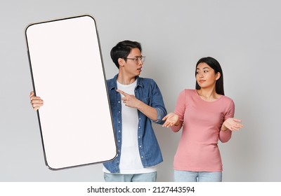 Another Life Online, Cheating Concept. Angry asian man checking hid girlfriend's mobile phone, showing provocative messages asking woman for explanation pointing at empty screen, lady spreading hands
