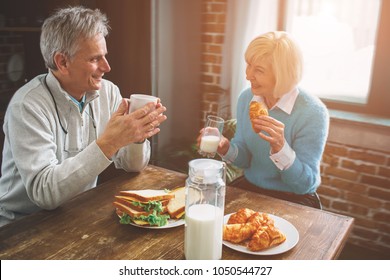 Another Picture Of Nature Old People Sitting In The Kitchen. THey Are Drinking Milk And Talking To Each Other. They Are Enjoying Company Of One Another.