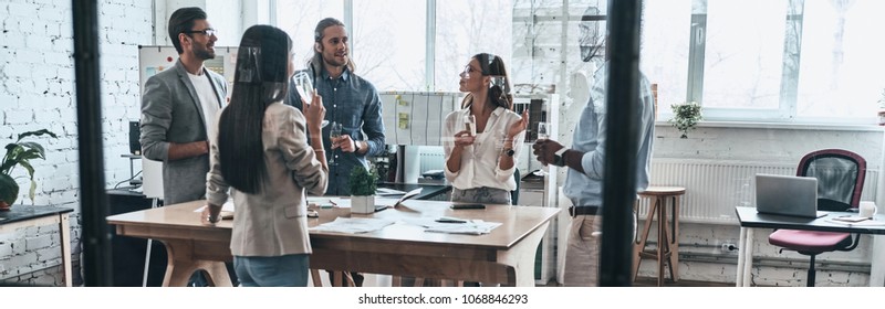 Another project well done. Full length of young business people drinking champagne and smiling while standing behind the glass wall in the board room