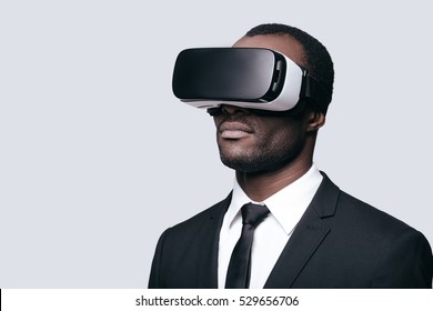 Another reality is here! Handsome young African man in VR headset standing against grey background