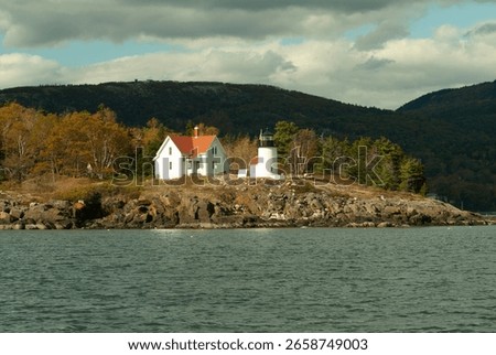 Another viewpoint of a charming lighthouse overlooking calm waters, framed by colorful autumn trees. This image emphasizes tranquility and the beauty of coastal life.