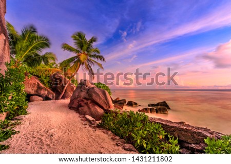 Anse Source d'Argent in Seychelles, La Digue with dramatic colorful sky at eveing. Shaped rock stone of granite, palm trees and seashore. Source d'Argent Beach paradise of Seychelles. Long exposition.
