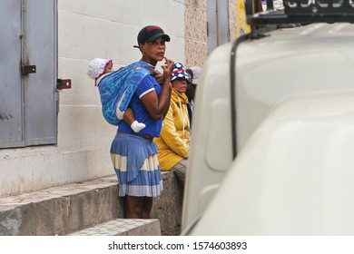 Antananarivo, Madagascar - April 24, 2019: Unknown Malagasy Woman Carries Her Baby In Wrap Sling Over Her Shoulder. People On Madagascar Are Poor, Most Women Can't Afford To Stay Home With Children.