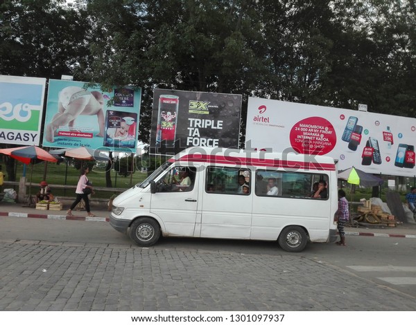 Antananarivo, Madagascar - January 20, 2019: public\
transportation bus in front of a lot of ads billboard; street shop\
in the sidewalk 
