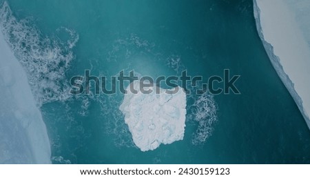 Antarctic iceberg top down view washed by blue ocean waves. Melted glacier in ice canyon of South Pole. Breathtaking harmony of untouched nature. Global warming. Climate change. High angle drone shot.