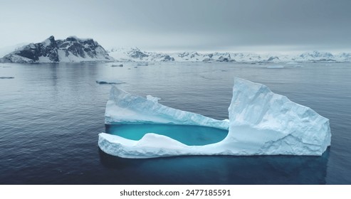 Antarctic melting iceberg floating in cold blue water, aerial. Snow-covered mountains in background. Melting glacier drift in Polar ocean. Ecology, melting ice, climate change, global warming concept - Powered by Shutterstock