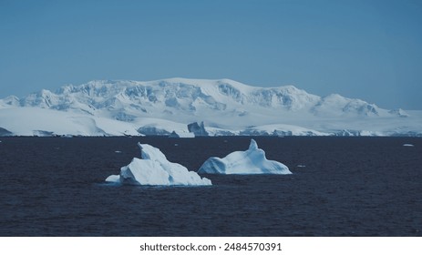 Antarctica Blue Frozen Scenery Two Icebergs Float with Gentle Snow Sloping Soft Mountain in Background Low Mist Clouds. Beautiful Landscape. - Powered by Shutterstock