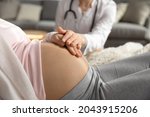 Antenatal care. Female doctor family therapist ob-gyn support comfort help young pregnant woman patient. Medic worker touching hand of expectant mother caressing her belly on checkup. Close up view