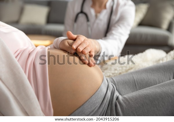 Antenatal care. Female doctor family therapist\
ob-gyn support comfort help young pregnant woman patient. Medic\
worker touching hand of expectant mother caressing her belly on\
checkup. Close up\
view