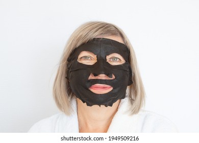 Anti Age Concept. Senior Woman Applies A Black Cosmetic Mask To Her Face. Mature Woman Face After Spa Treatment. Beauty Spa Treatment. Plastic Surgery Clinic, New Senior, Cosmetology