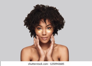 Anti Aging. Attractive Young African Woman Applying Medical Eye Patch And Smiling While Standing Against Grey Background