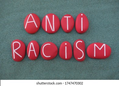Anti Racism, social issue slogan text composed with red colored stone letters over green sand