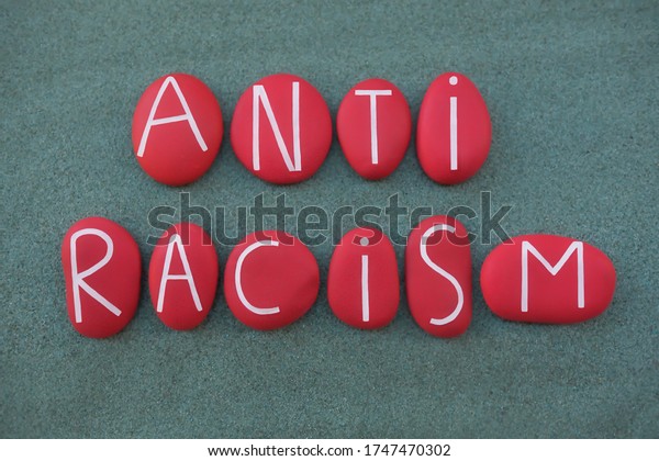 Anti Racism, social issue slogan\
text composed with red colored stone letters over green\
sand