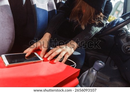 Anti theft system problem concept. Burglar thief man wearing black clothes breaking into car, stealing smartphone and red shopping bag