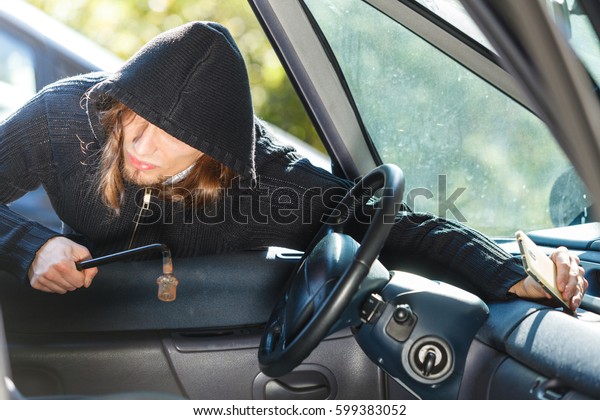 Anti\
theft system problem concept. Burglar thief man wearing black\
clothes breaking into car and stealing\
smartphone