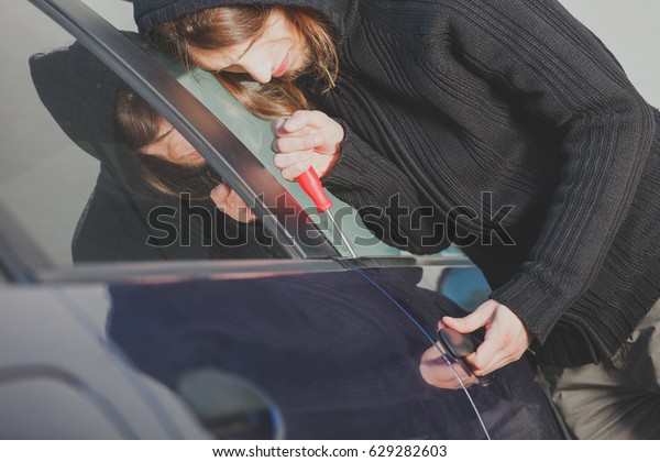 Anti theft system\
problem concept. Thieft man dressed in black holding screwdriver\
trying to break into car
