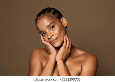 Antiage skincare concept. Beautiful black middle aged woman with flawless skin touching face and looking at camera, aged lady standing over brown studio background - Powered by Shutterstock