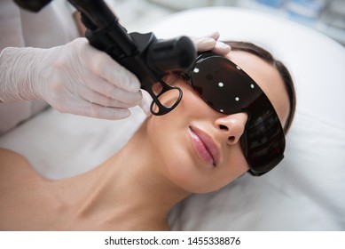 Anti-aging body treatment. Close up top angle portrait of pretty smiling woman in eyeglasses having laser fractional rejuvenation of face in cheek zone - Shutterstock ID 1455338876