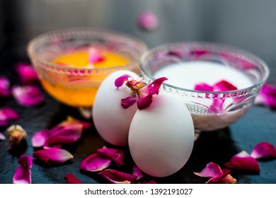 Anti-aging Face Pack I.e.  Milk And Egg Face Pack In A Glass Bowl On Shiny Black Surface With Some Rose Petals And Entire Of Its Constituents With It.