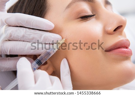 Anti-aging face treatment. Close up side on portrait of young smiling pretty woman relaxing on rejuvenation procedure of cheek bone zone by specialist