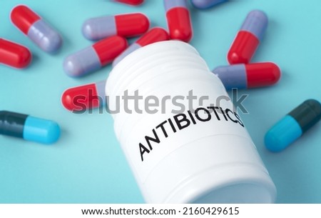 Antibiotic medicine concept, antibiotics bottle with pills spilled out, closeup on blue background