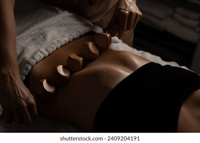 Anti-cellulite massage on the stomach using wooden objects. Massage salon in a dark room.