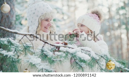 In anticipation of Christmas, Mom and a little girl decorate in the yard of the house a Christmas tree with toy balls
