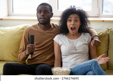 In Anticipation Of Victory Favorite Sports Team, Motionless African Couple Fans Gawp At TV Screen Waiting For Goal. American Spouses Sit On Couch Spend Weekend With Popcorn And Thriller Movie Concept