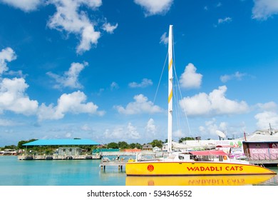 Antigua, Antigua And Barbuda - December 13, 2016: Modern Yellow Yacht Or Sailing Boat Or Marine Vessel Under Bare Poles At Moorage At Pier In Sea Dock Or Bay On Sunny Day On Blue Sky