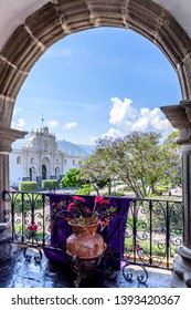 Antigua, Guatemala - April 10, 2019: View Of San José Cathedral & Central Park Through Arch On City Hall Terrace With Purple Lent Banner In Colonial City & UNESCO World Heritage Site Of Antigua.