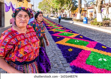 Antigua, Guatemala -  April 14, 2019: Maya ladies by dyed sawdust Palm Sunday procession carpet in UNESCO World Heritage Site with famed Holy Week celebrations.