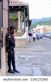 Antigua / Guatemala - July 17 2018: Police Officer Talking On The Phone While Guarding The Cobblestone Street In Guatemala.  