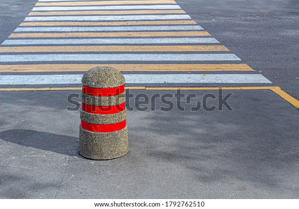 Anti-Parking concrete column with three red\
fluorescent stripes, the column is covered with rubble on top and\
stands next to the ground pedestrian\
crossing