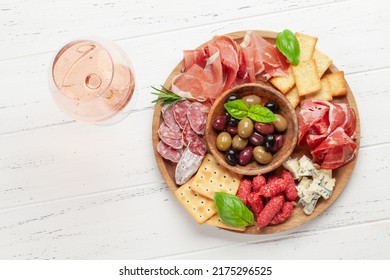 Antipasto board with prosciutto, salami, crackers, cheese, nuts, olives and rose wine. Top view flat lay - Powered by Shutterstock