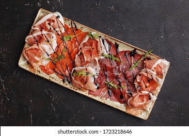 Antipasto Meat Platter. Cold Cuts. Deli Meat Platter. Set Of Assorted Sliced Meat And Sausage Garnished With Arugula And Balsamic Vinegar Over Dark Concrete Background. Overhead View, Copy Space