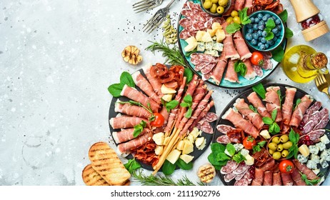 Antipasto plate of cold meat, prosciutto, parmesan cheese and blue cheese with grissini bread sticks. On a stone background. - Shutterstock ID 2111902796