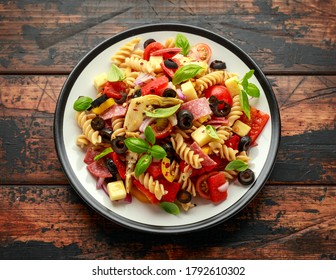 Antipasto Salad With Pasta, Tomato, Olives, Red Onion, Bell Pepper, Salami, Cheese Artichoke And Basil On Wooden Table