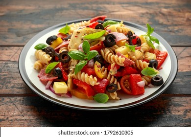 Antipasto Salad With Pasta, Tomato, Olives, Red Onion, Bell Pepper, Salami, Cheese Artichoke And Basil On Wooden Table