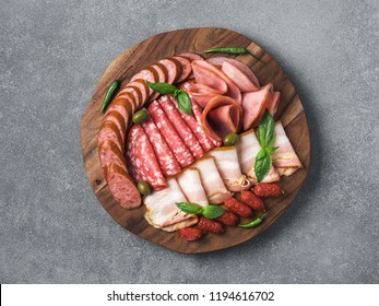 Antipasto set platter wooden plate on gray stone. Cold smoked meat plate with sausage, sliced ham,prosciutto,bacon,olives,basil. Appetizer on wooden tray cut tree sawed imitation. Copy space. Top view